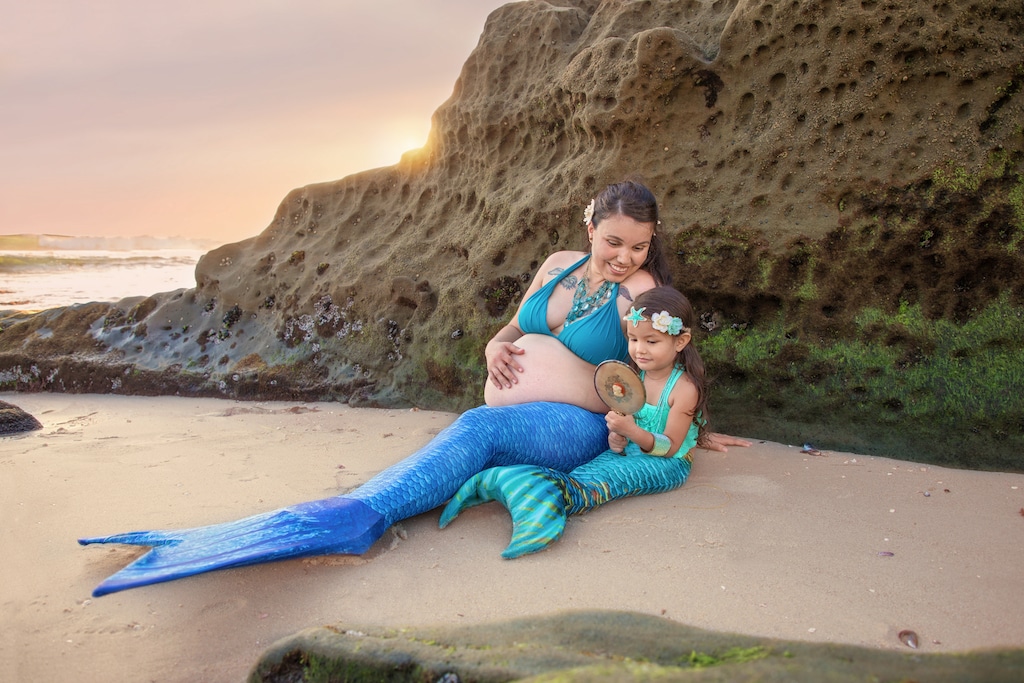 Pregnant mermaid and her daughter on a beach in San Diego