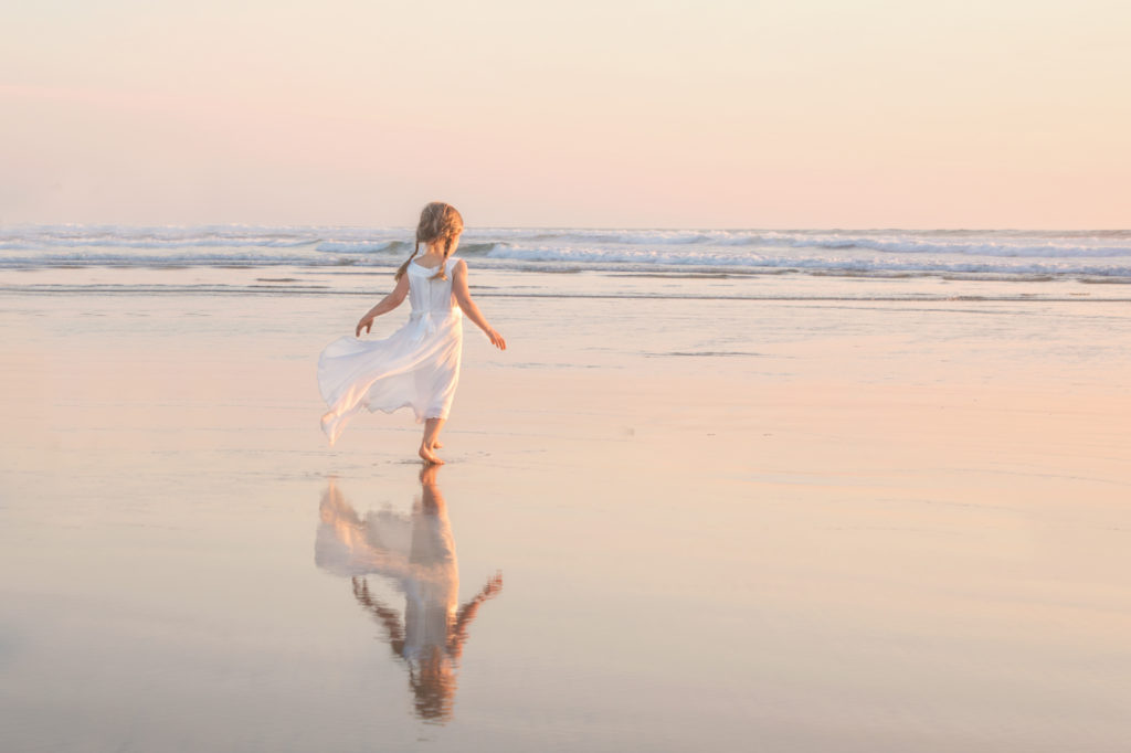 Little girl in a white dress walking on the sand at low tide in San Diego