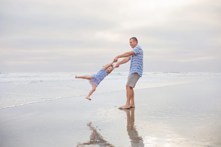 Father swinging daughter around at a San Diego beach