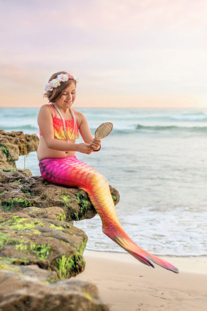 San Diego Mermaid looking in a mirror on a rock