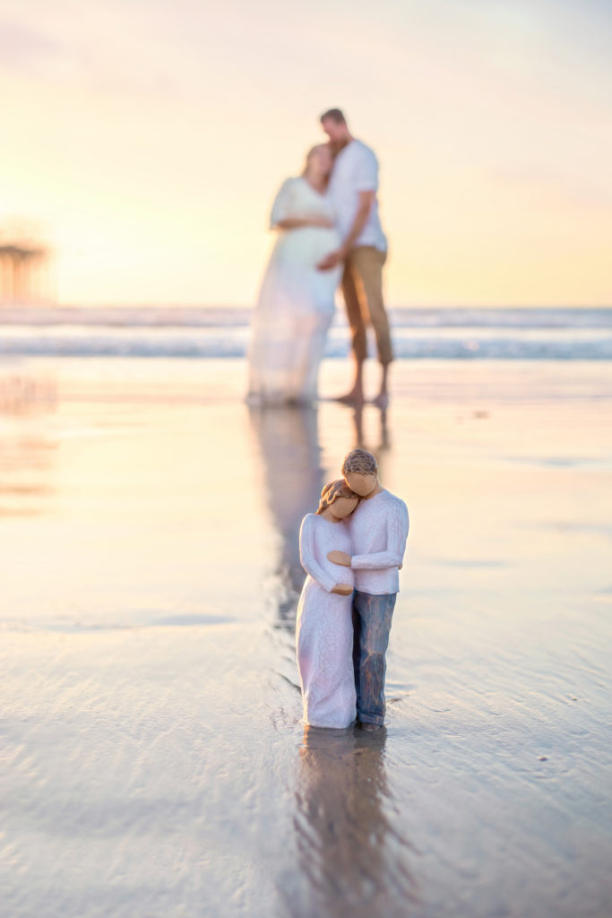 Pregnant couple pose on the beach at Scripps Pier