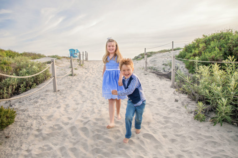 Children holding hands running down sand dunes at South Ponto Beach