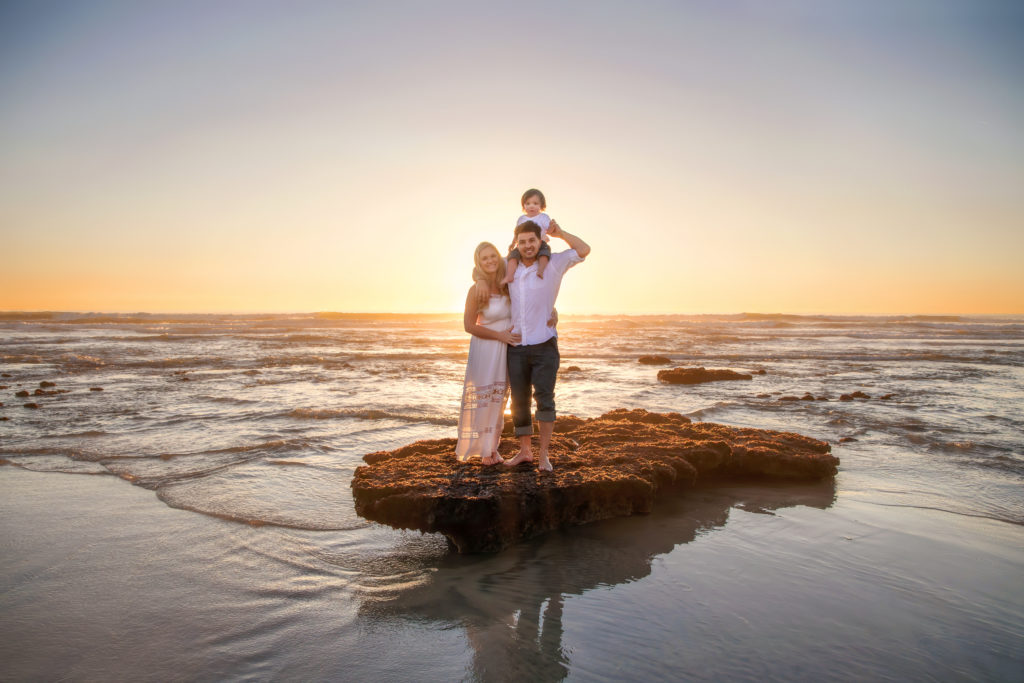 Family standing on a rock in the water at sunset.