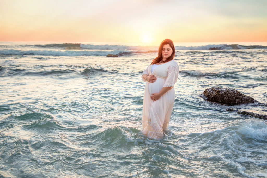 Pregnant woman standing in the waves at sunset