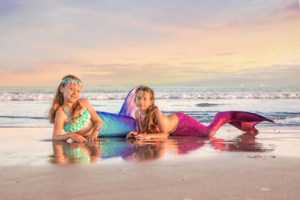 Two little pink and purple mermaids on the beach in San Diego at sunset