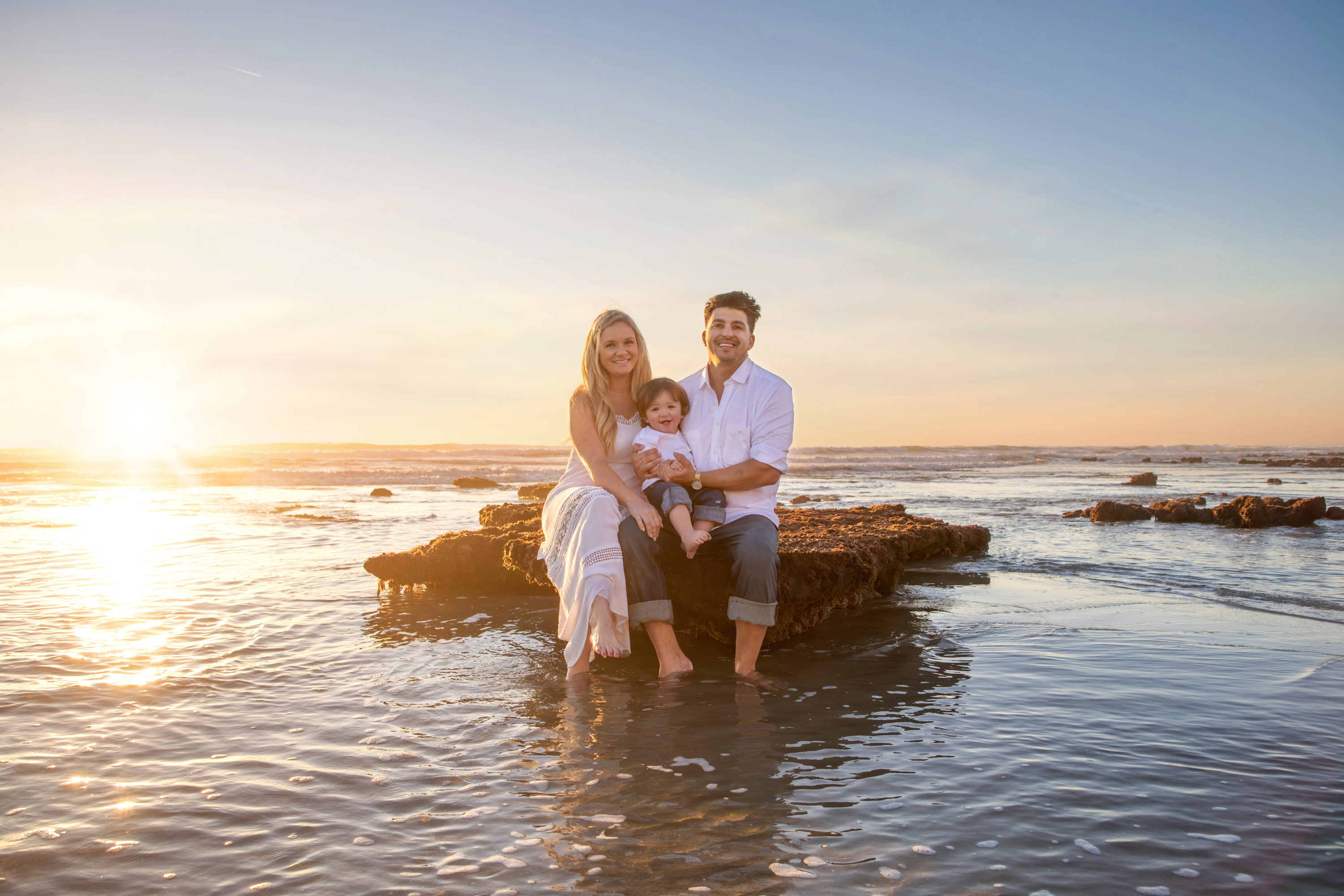 Family sitting on a rock in the water at sunset