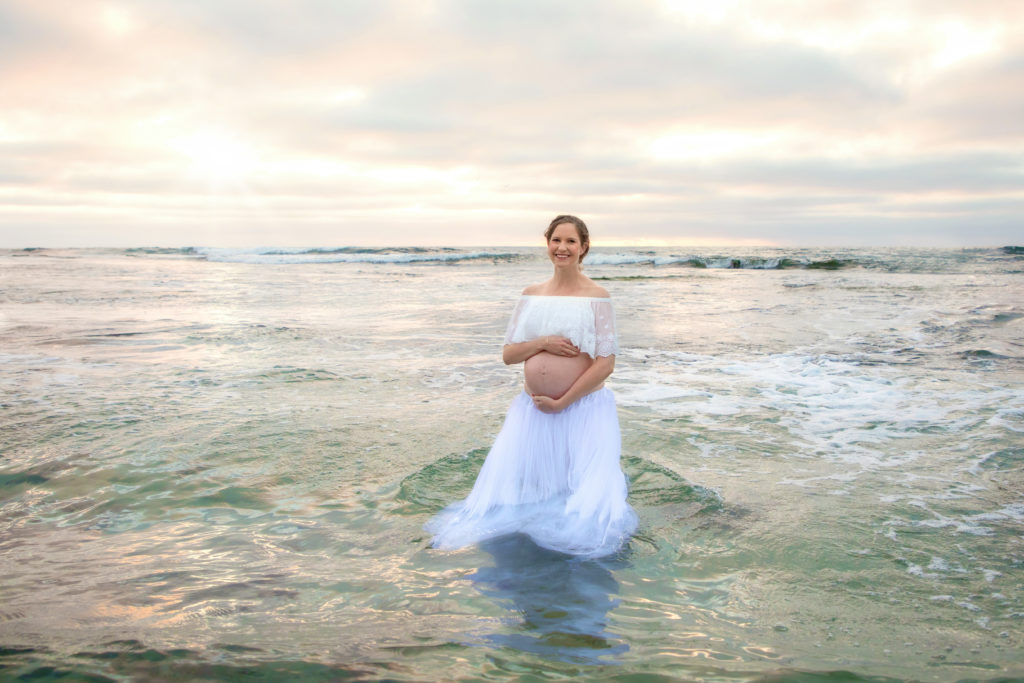Maternity shoot with mother to be standing in the ocean at sunset