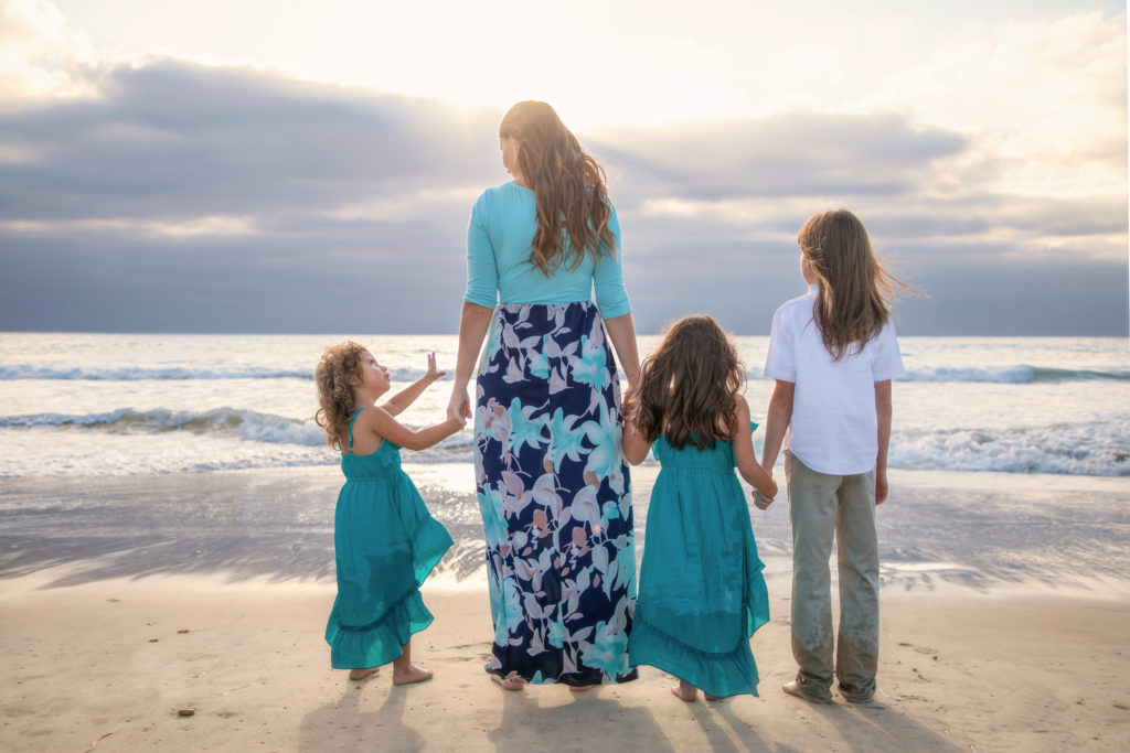 Family holding hands watching the sunset on a San Diego beach.