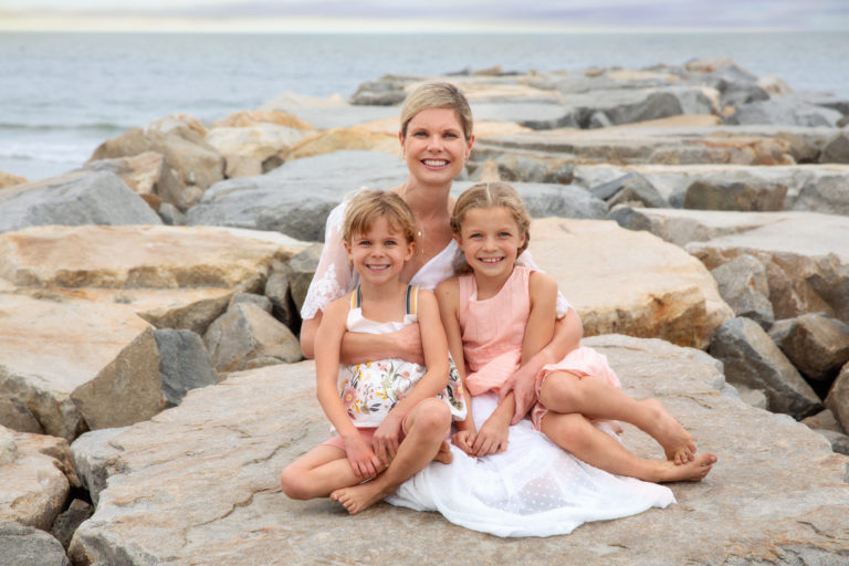 Mother in white dress sitting on San Diego beach with her two little girls